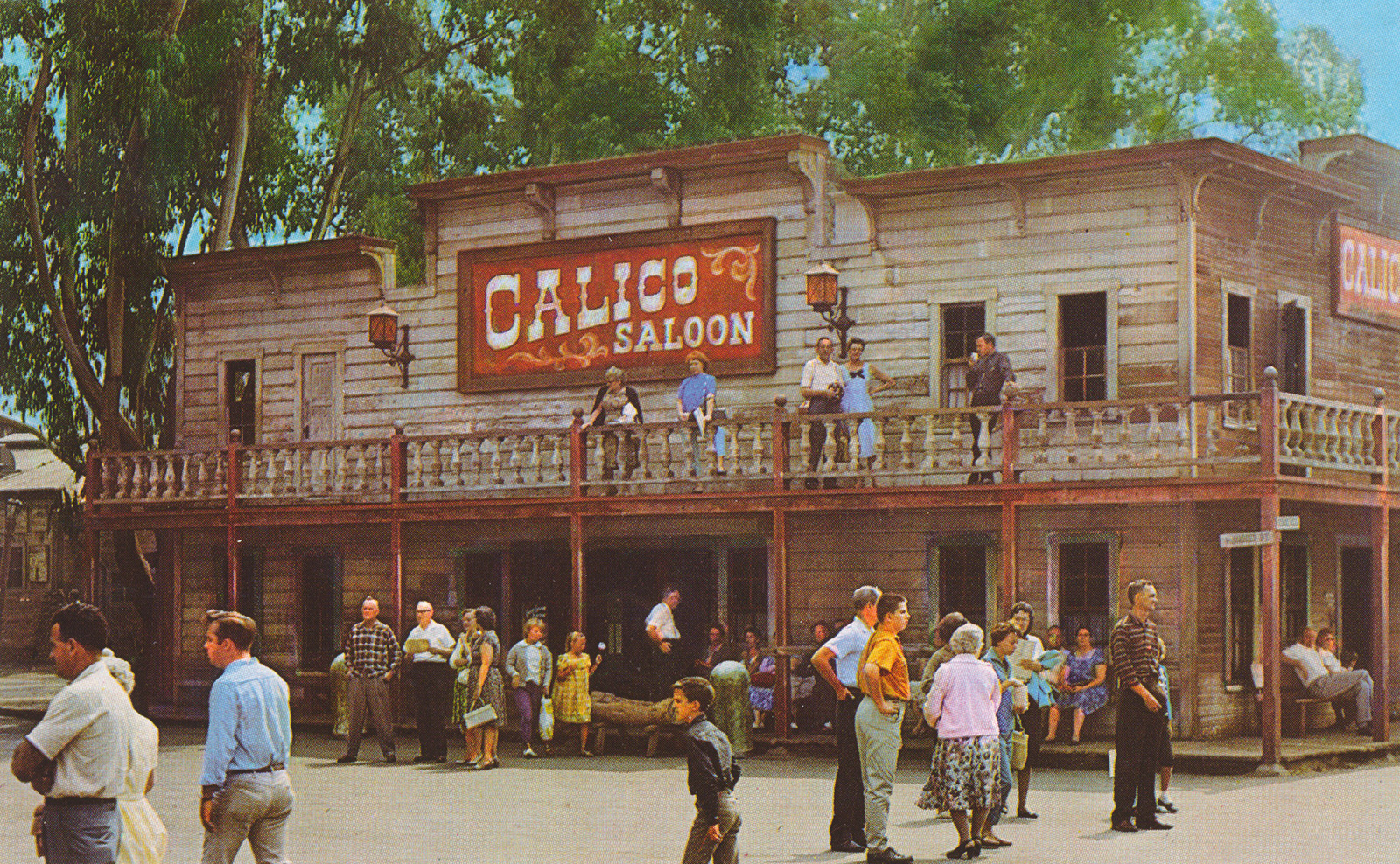 The Calico Saloon, a grey two story building with red trim. Guests stand outside and on the balcony.