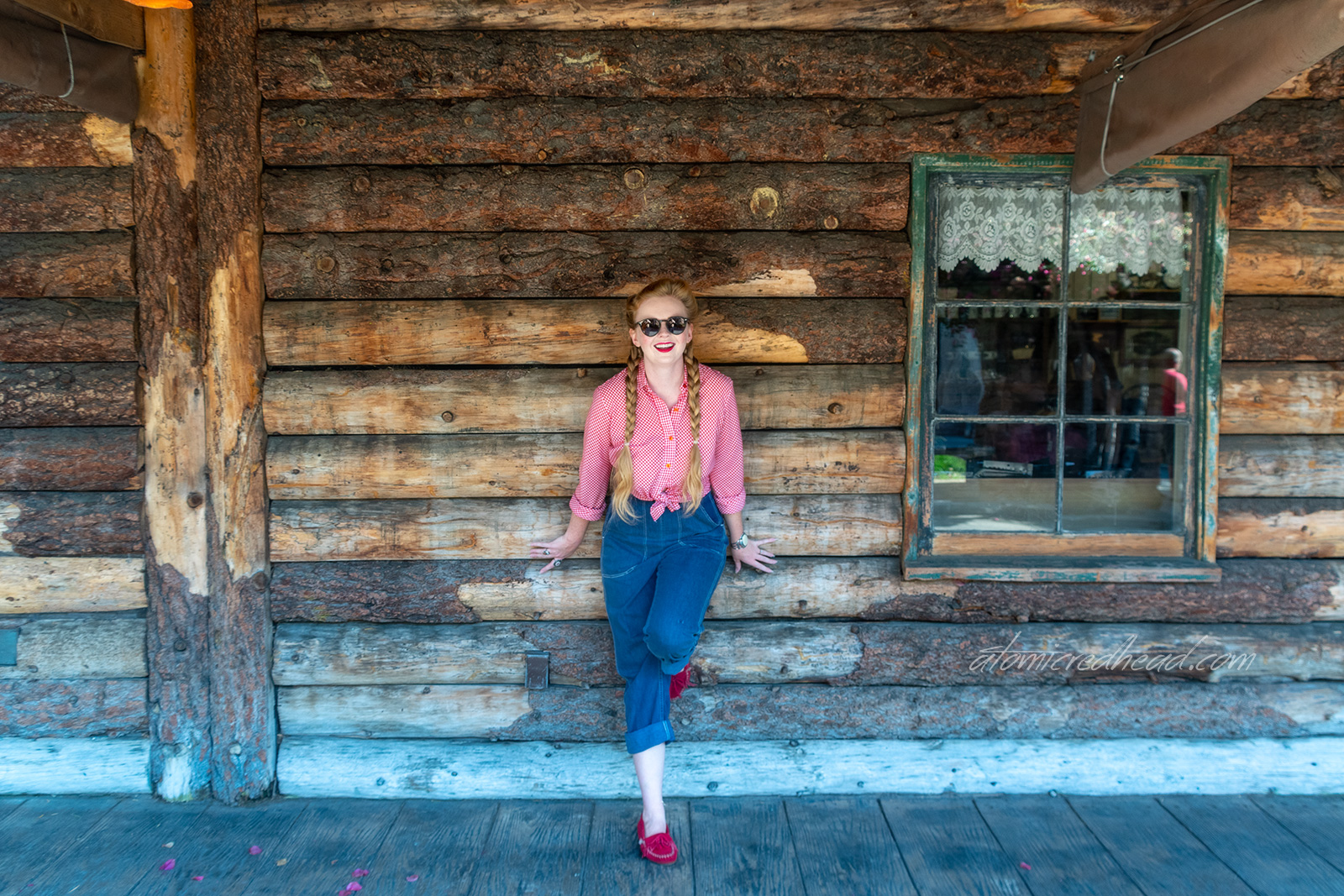 Myself standing in front of a building made of logs, wearing a red and white gingham shirt, and blue jeans.