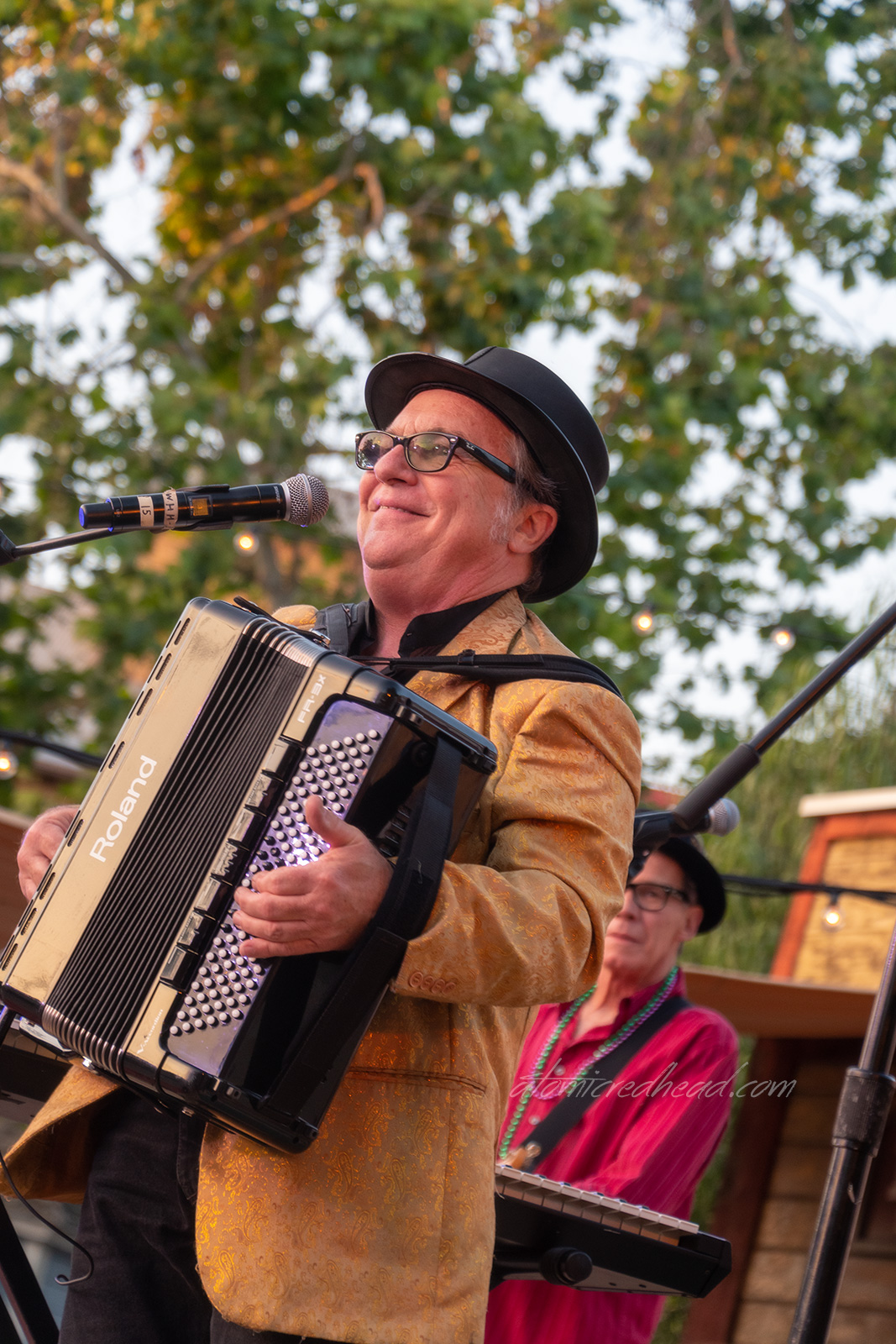 The accordion player of the band Doug Legacy & the Zydeco Cajun Party Band, wears a gold jacket and black hat.