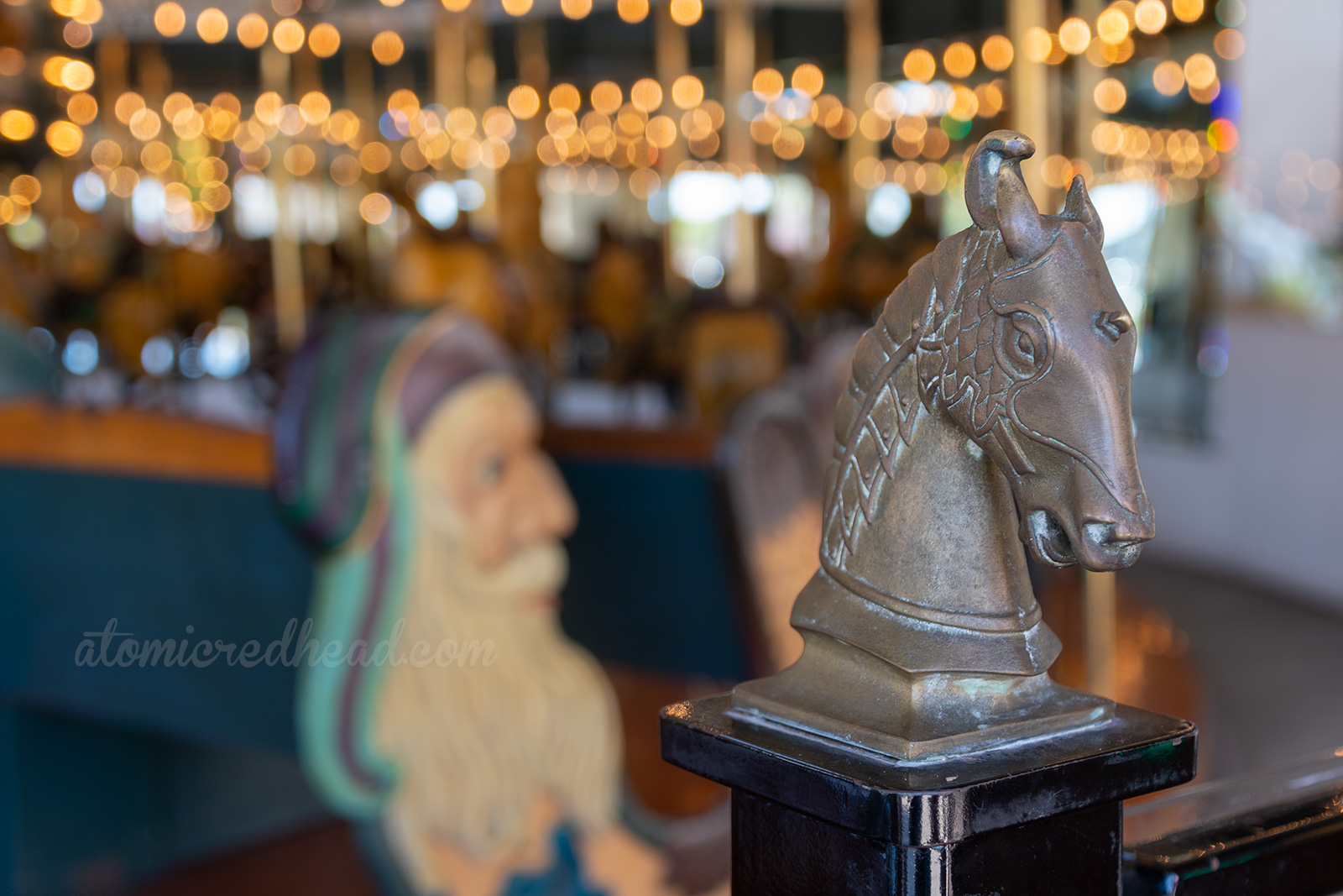 Closeup of a horse head that sits atop on the of the rails of the carousel. 