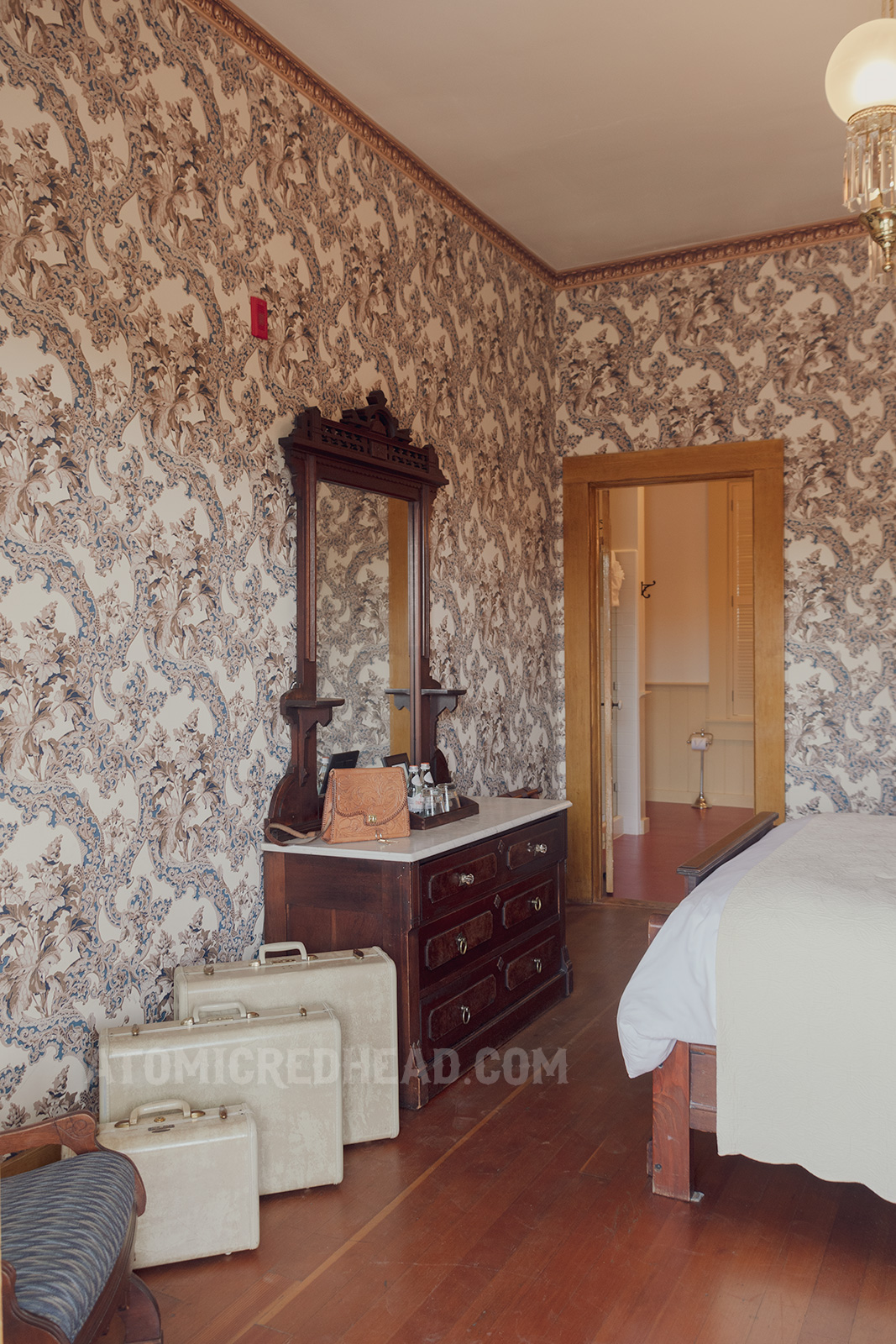 Interior of our room. An antique oak dresser sits against a wall. Floral wallpaper in tan, blue, and white wraps around the room.