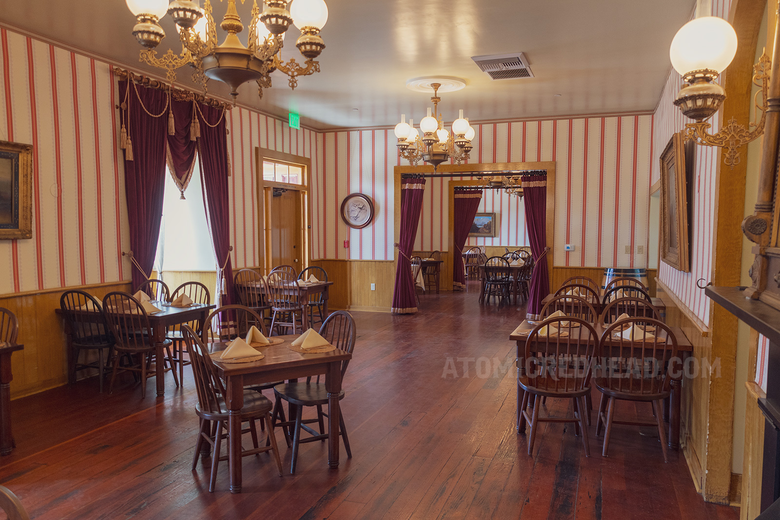 Interior of the tea room, with antique oak tables, red velvet curtains with gold trim, brass and glass chandeliers, and red and white stripe wallpaper.