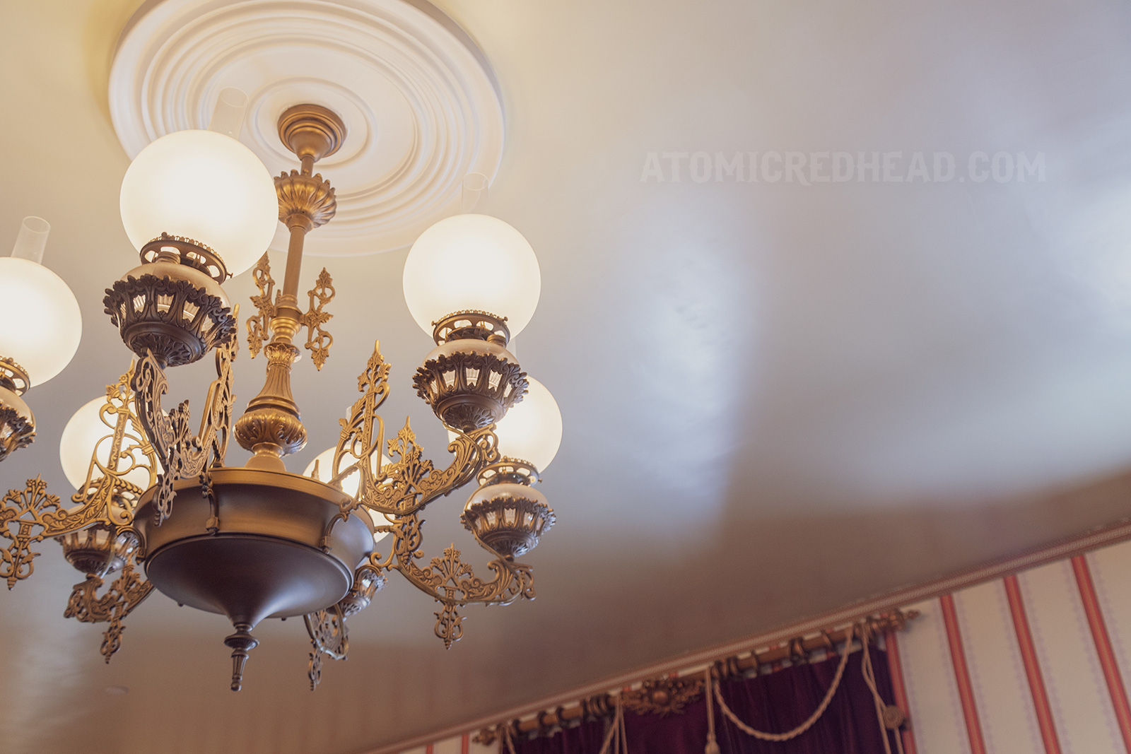 Close up of the brass and glass chandelier, scroll works details the brass which large white globe like shades sit upon.