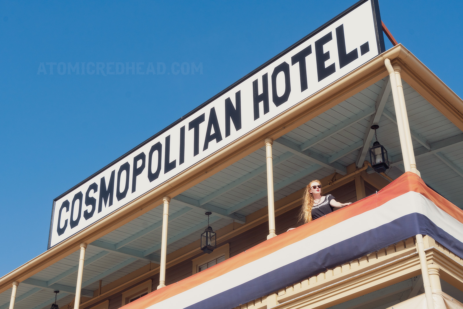 Myself standing on the outer balcony of the hotel, wearing a black dress with silver trim. A massive white sign reads "Cosmopolitan Hotel" in black letters.