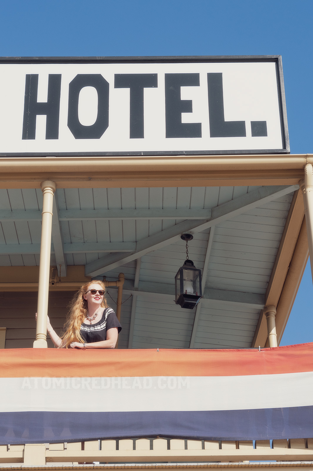 Myself standing on the outer balcony of the hotel, wearing a black dress with silver trim. A massive white sign reads "Cosmopolitan Hotel" in black letters.