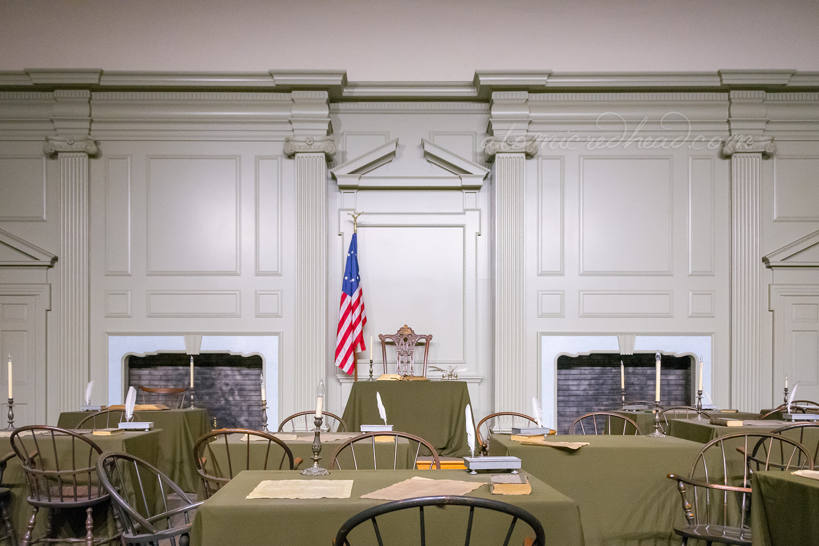 Inside the singing room, a chair and small desk sit against the back wall. The walls are painted a pale green color. In front a small collection of tables and chairs, atop each table are quills and parchment.