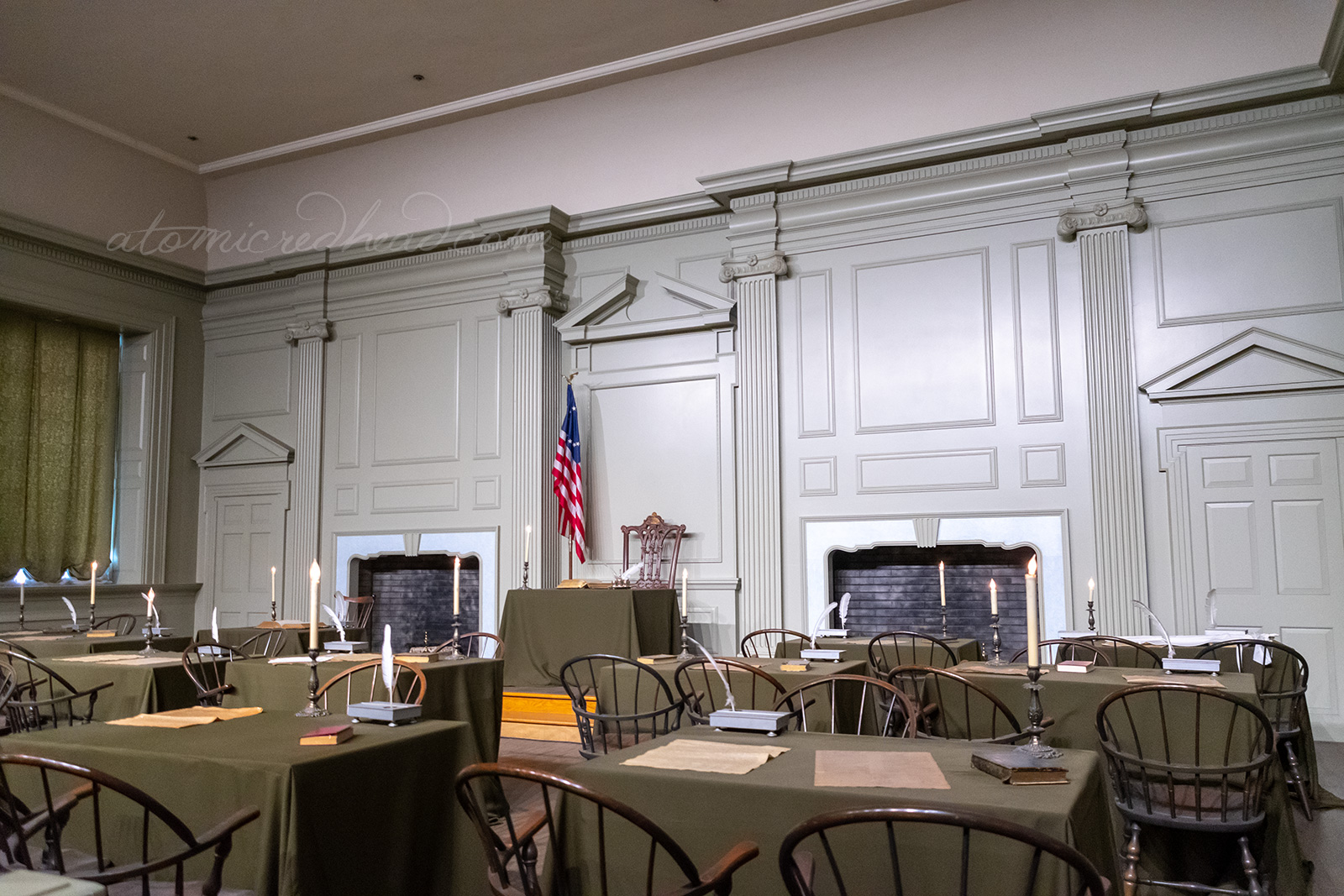 Inside the singing room, a chair and small desk sit against the back wall. The walls are painted a pale green color. In front a small collection of tables and chairs, atop each table are quills and parchment.