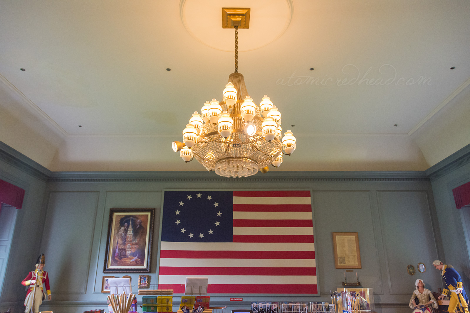 Inside the gift shop portion of Independence Hall. A massive flag, the original version, hangs on the wall. A chandelier hangs from the ceiling.