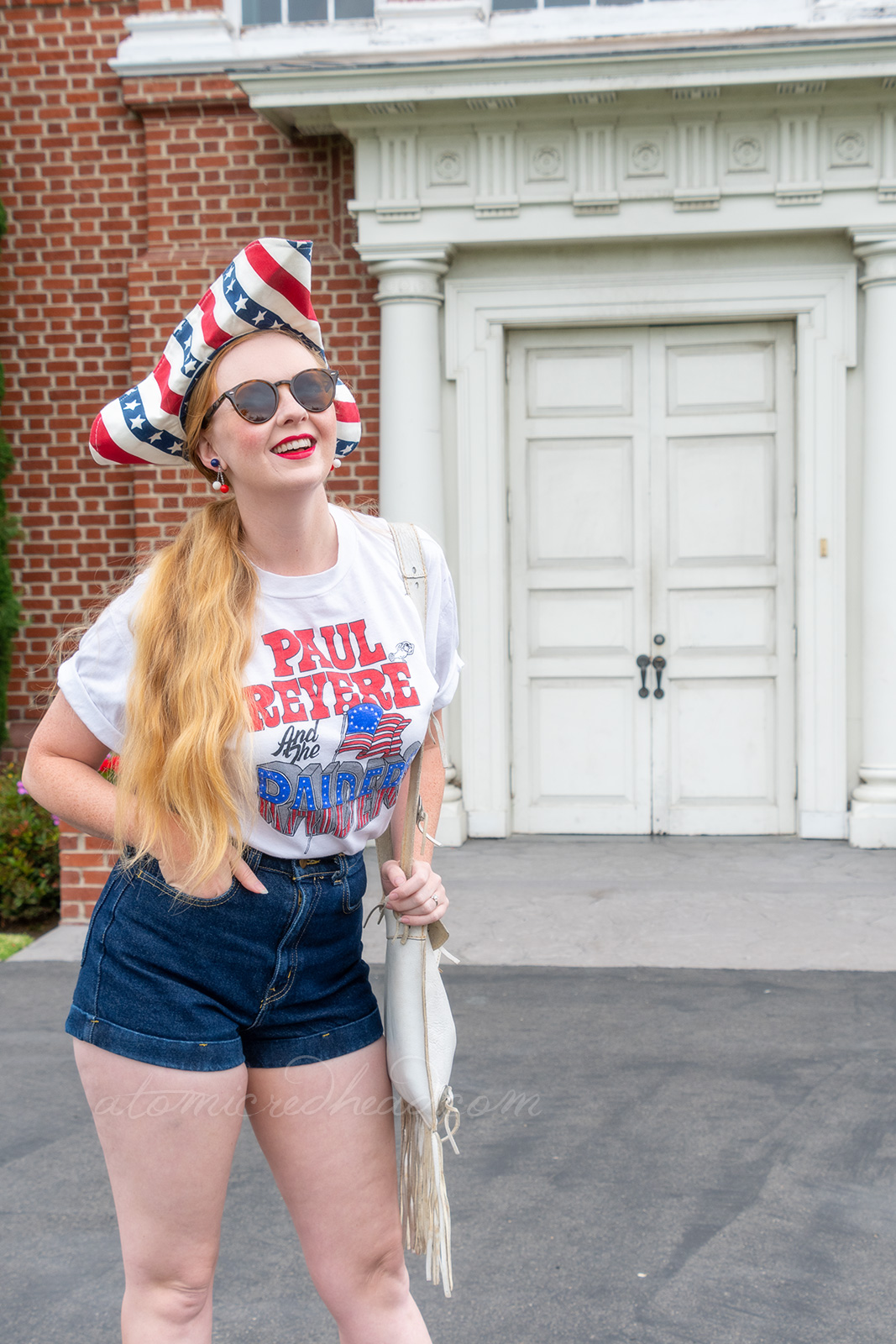 Myself standing outside Independence Hall, a red brick building with white windows and doors, wearing a tricorn hat of red, white and blue stripes, a white t-shirt reading "Paul Revere and the Raiders" with the original flag jutting from the "Raiders" portion, and jean shorts, and platform shoes features red and white stripes and blue with white stars.
