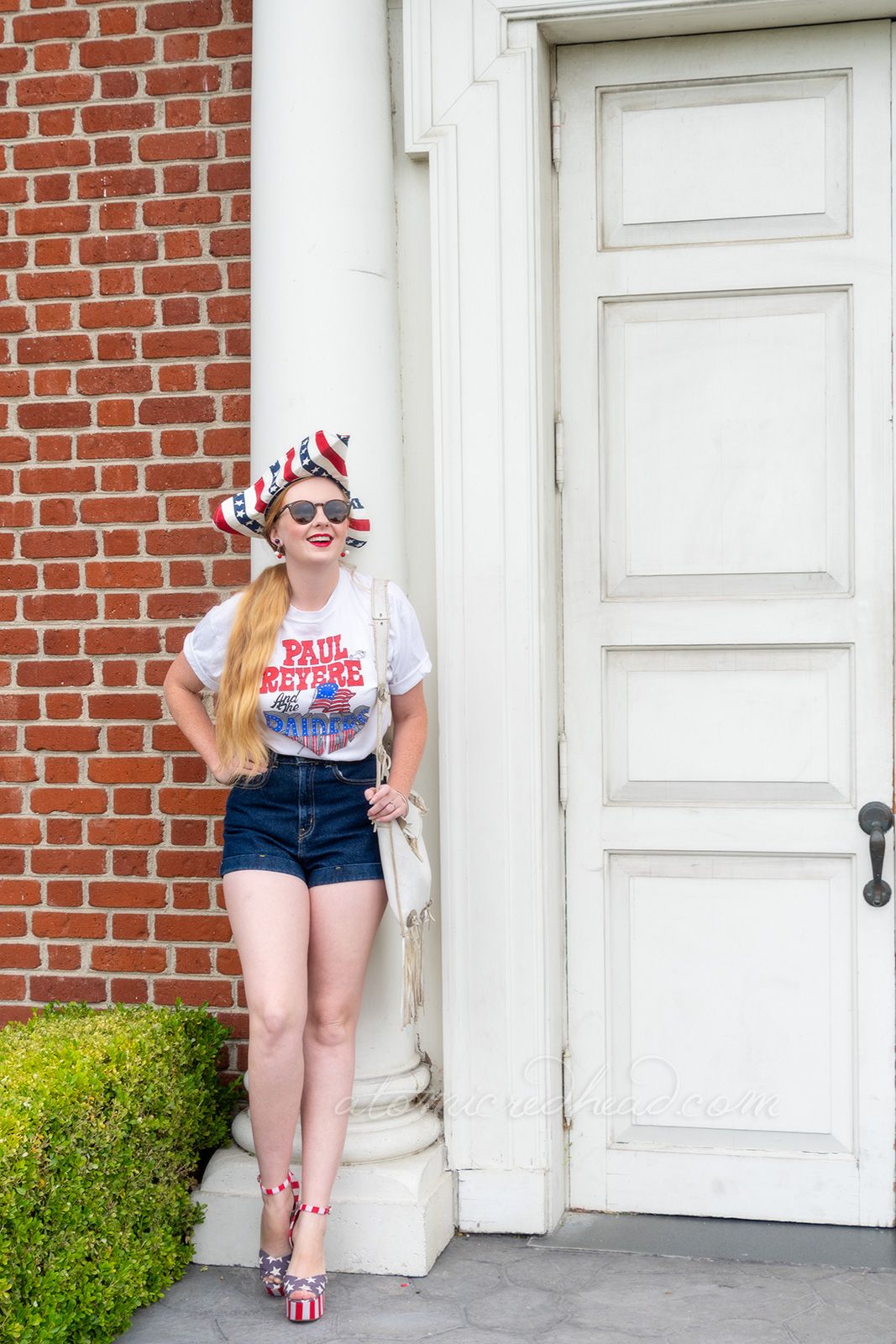 Myself standing outside Independence Hall, a red brick building with white windows and doors, wearing a tricorn hat of red, white and blue stripes, a white t-shirt reading "Paul Revere and the Raiders" with the original flag jutting from the "Raiders" portion, and jean shorts, and platform shoes features red and white stripes and blue with white stars.