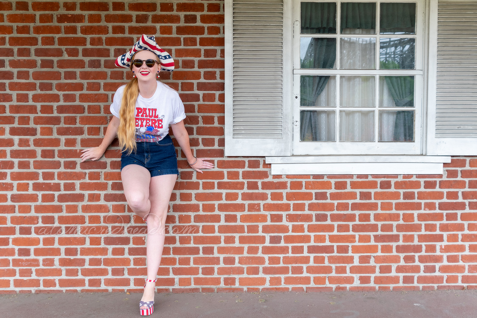 Myself standing outside Independence Hall, a red brick building with white windows and doors, wearing a tricorn hat of red, white and blue stripes, a white t-shirt reading "Paul Revere and the Raiders" with the original flag jutting from the "Raiders" portion, and jean shorts, and platform shoes features red and white stripes and blue with white stars.
