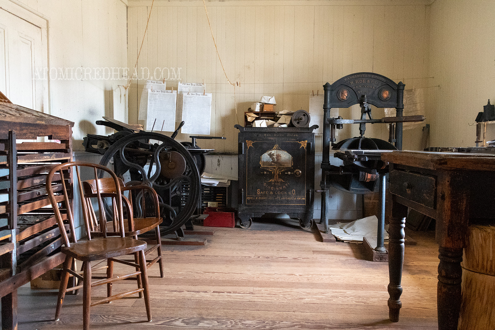 Interior of the print shop. An old type tray on the left, and massive old printing press on the right.