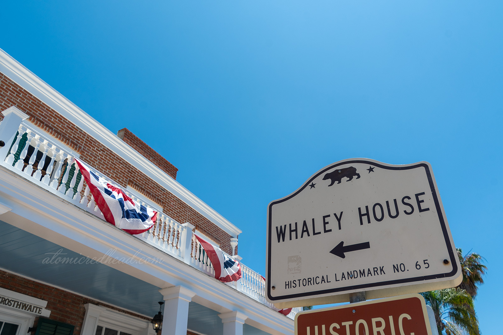 A brick house with white painted porch sits behind a sign reading "Whaley House Historic Landmark No. 65"
