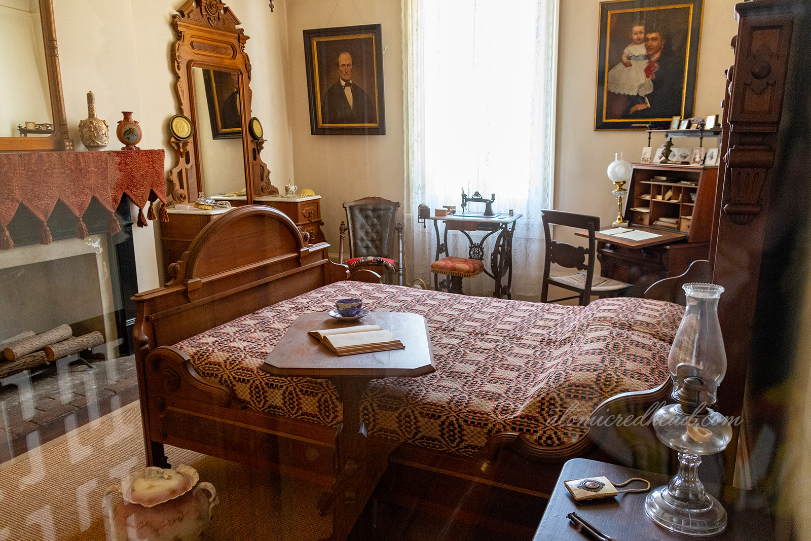 One of the bedrooms. A wood dresser with mirror sits in one corner, a dark wood desk in the other, and a full bed with red and white quilt in the center.