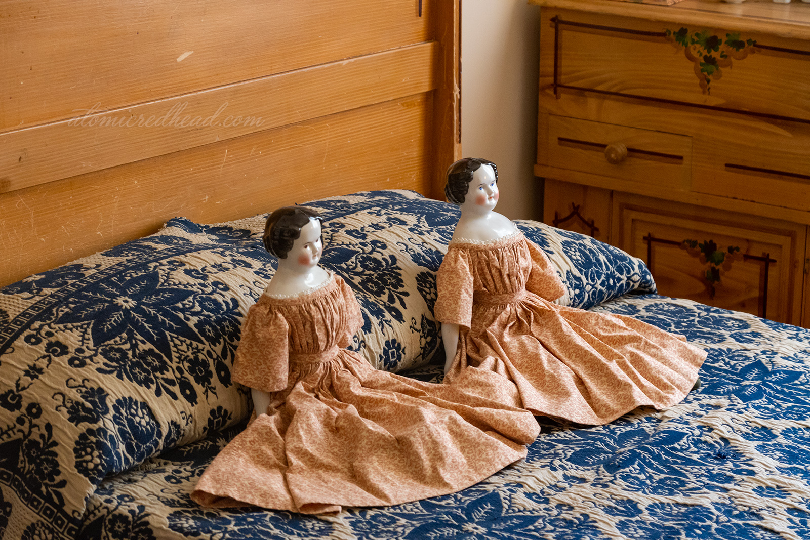 Two porcelain dolls with cloth dresses sit upon a blue and white bedspread in what was one of the children's rooms.