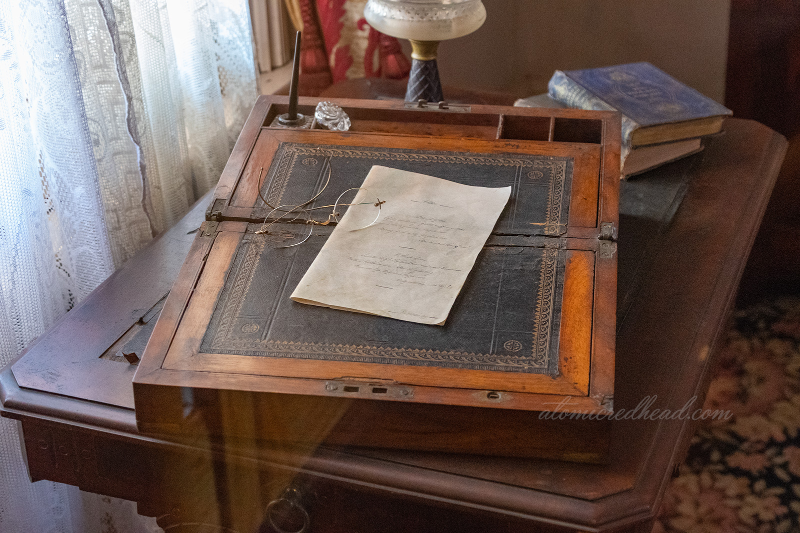 A portable writing desk sits atop a table, with a letter, and pair of glasses atop.