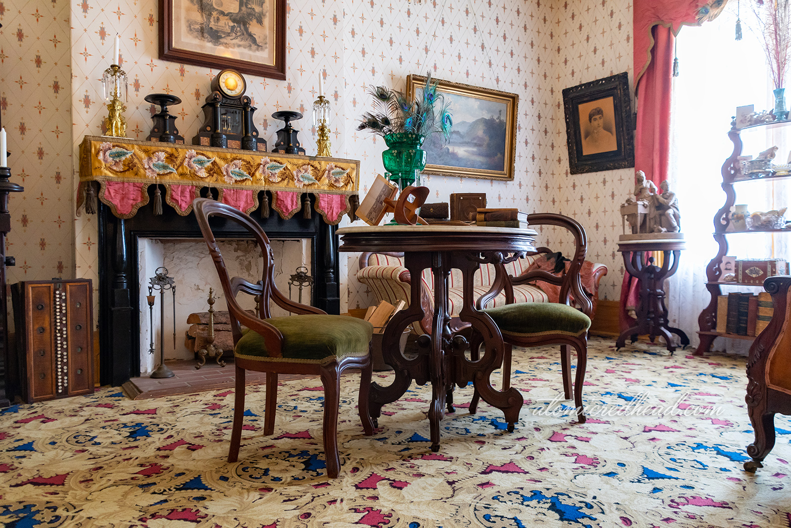 The parlor of the home, in front of the fireplace sits a small table and two chairs.