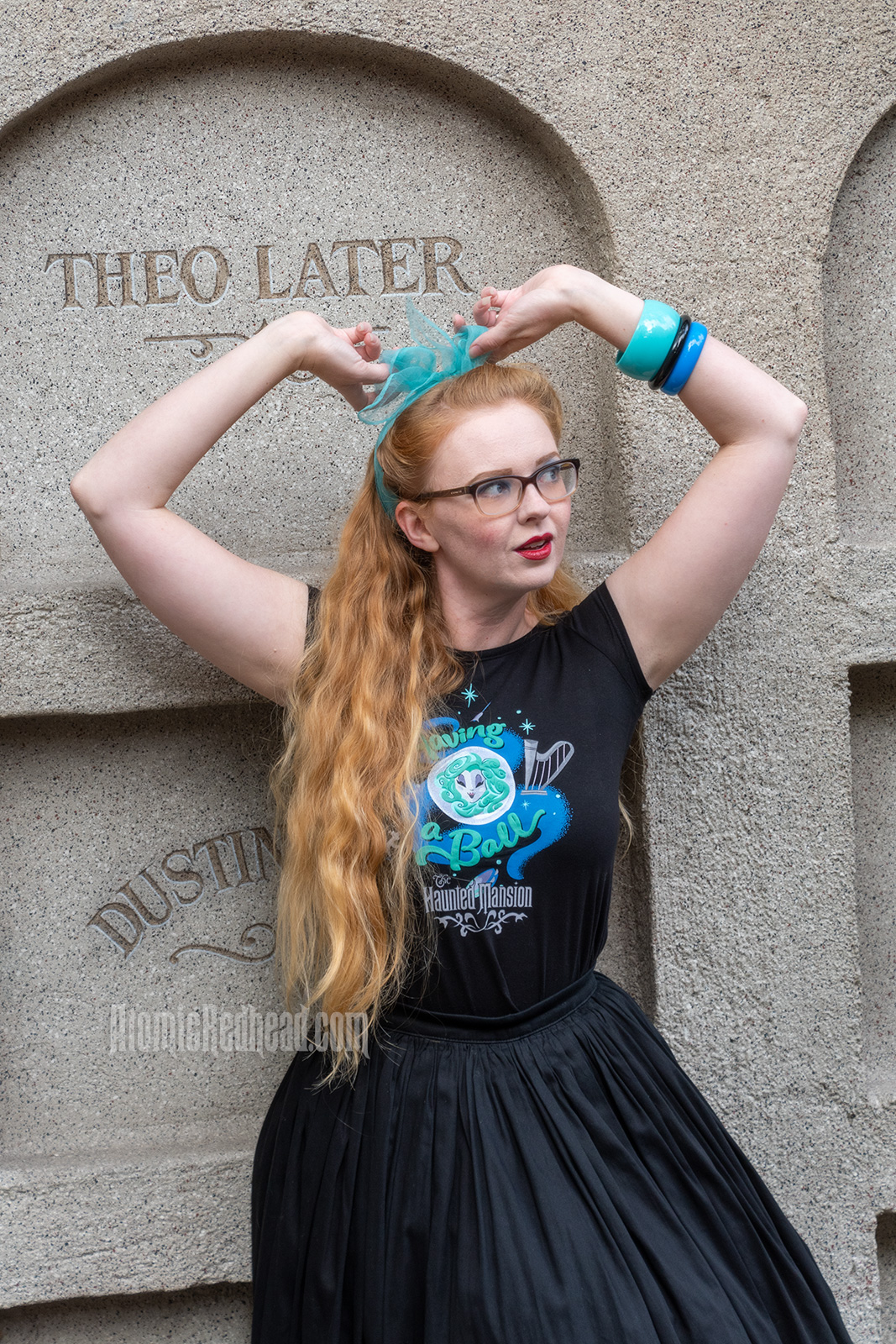 Myself standing in front of a faux mausoleum at the Haunted Mansion, wearing a black t-shirt with Madam Leota (a medium with her head floating in a crystal ball) and music instruments floating about on it, reading "Having a Ball" and a black full skirt.
