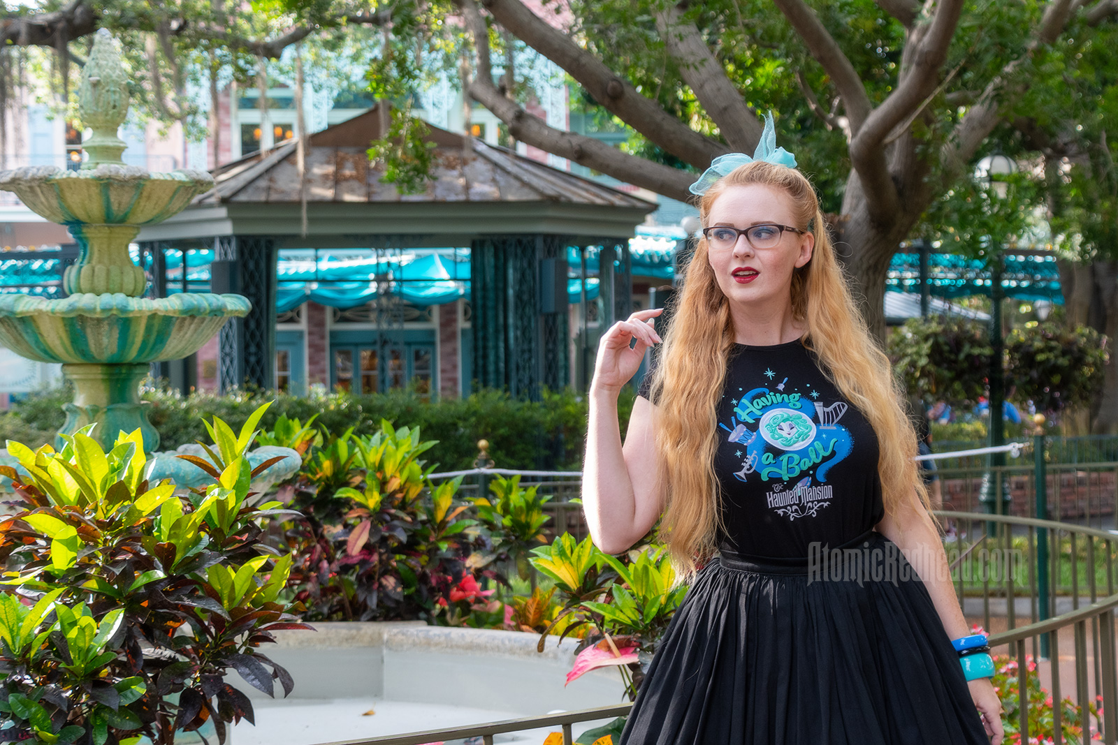 Myself standing in front of a fountain surrounded by trees dripping in Spanish moss, wearing a black t-shirt with Madam Leota (a medium with her head floating in a crystal ball) and music instruments floating about on it, reading "Having a Ball" and a black full skirt.