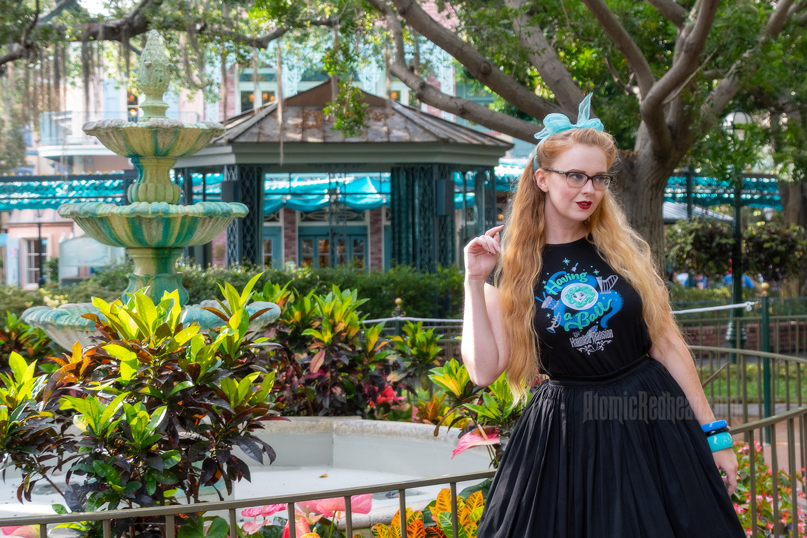 Myself standing in front of a fountain surrounded by trees dripping in Spanish moss, wearing a black t-shirt with Madam Leota (a medium with her head floating in a crystal ball) and music instruments floating about on it, reading "Having a Ball" and a black full skirt.