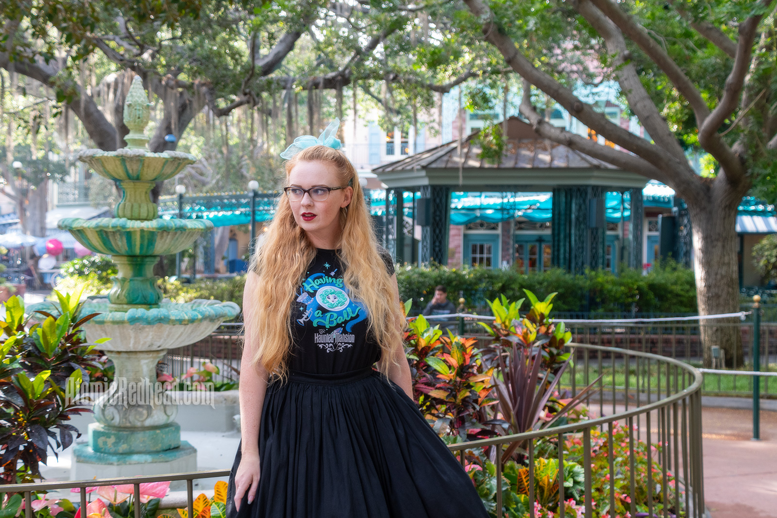 Myself standing in front of a fountain surrounded by trees dripping in Spanish moss, wearing a black t-shirt with Madam Leota (a medium with her head floating in a crystal ball) and music instruments floating about on it, reading "Having a Ball" and a black full skirt.