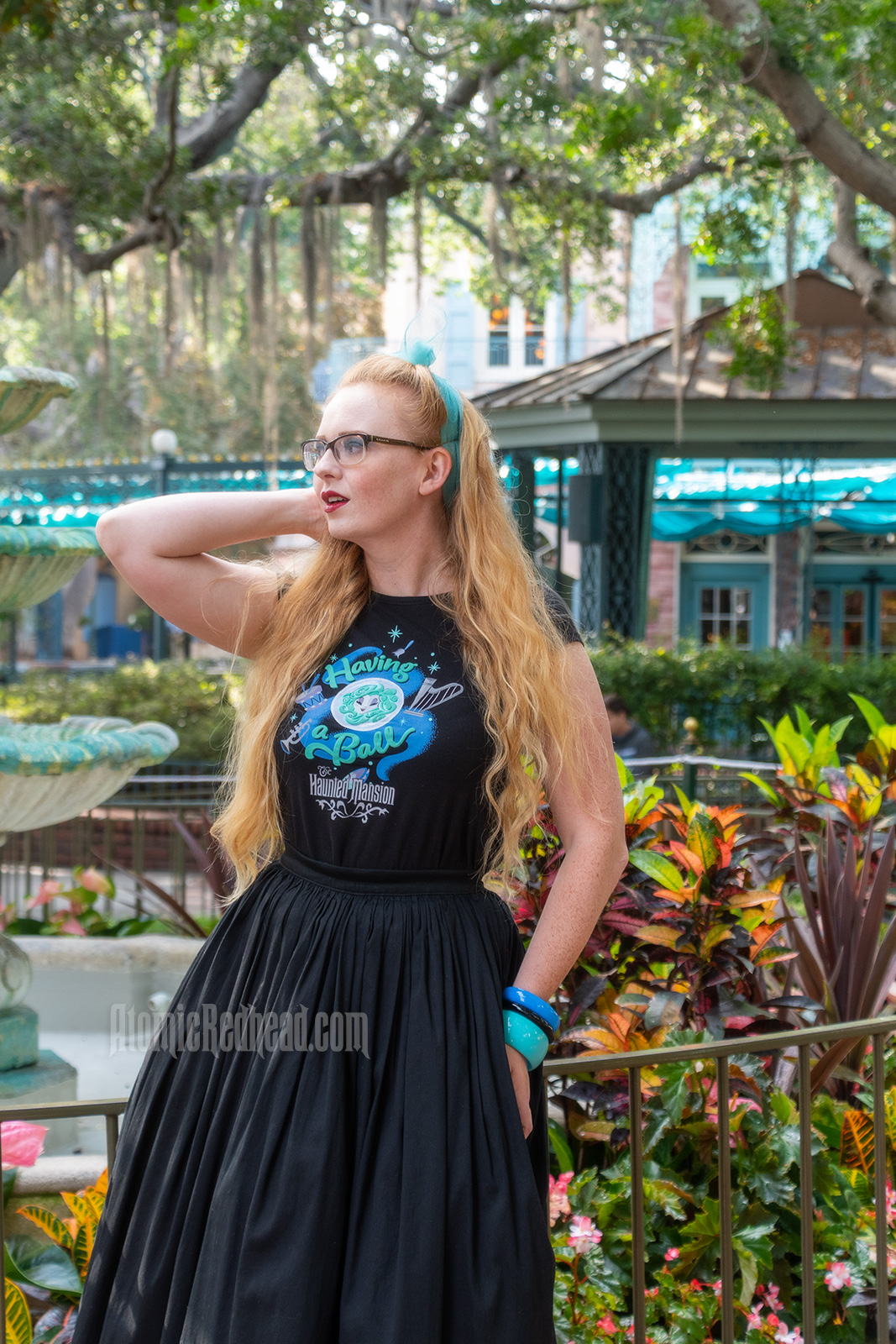 Myself standing in front of a fountain surrounded by trees dripping in Spanish moss, wearing a black t-shirt with Madam Leota (a medium with her head floating in a crystal ball) and music instruments floating about on it, reading "Having a Ball" and a black full skirt.