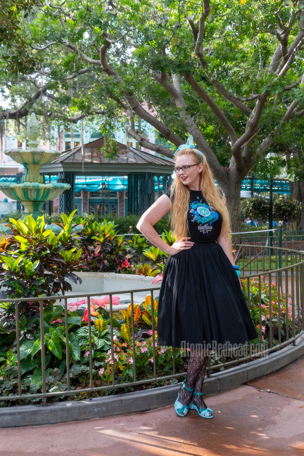 Myself standing in front of a fountain surrounded by trees dripping in Spanish moss, wearing a black t-shirt with Madam Leota (a medium with her head floating in a crystal ball) and music instruments floating about on it, reading "Having a Ball" and a black full skirt.
