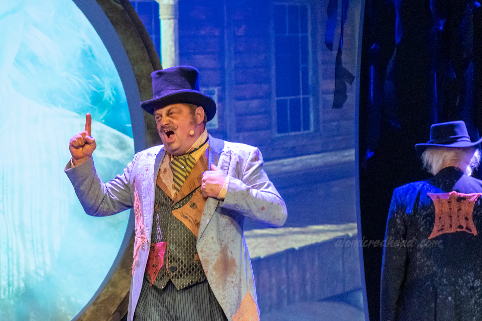 The Mayor of Calico raises a finger in concern for what is happening to the town, he is dressed in old western attire with an overcoat, vest, tie, and top hat.