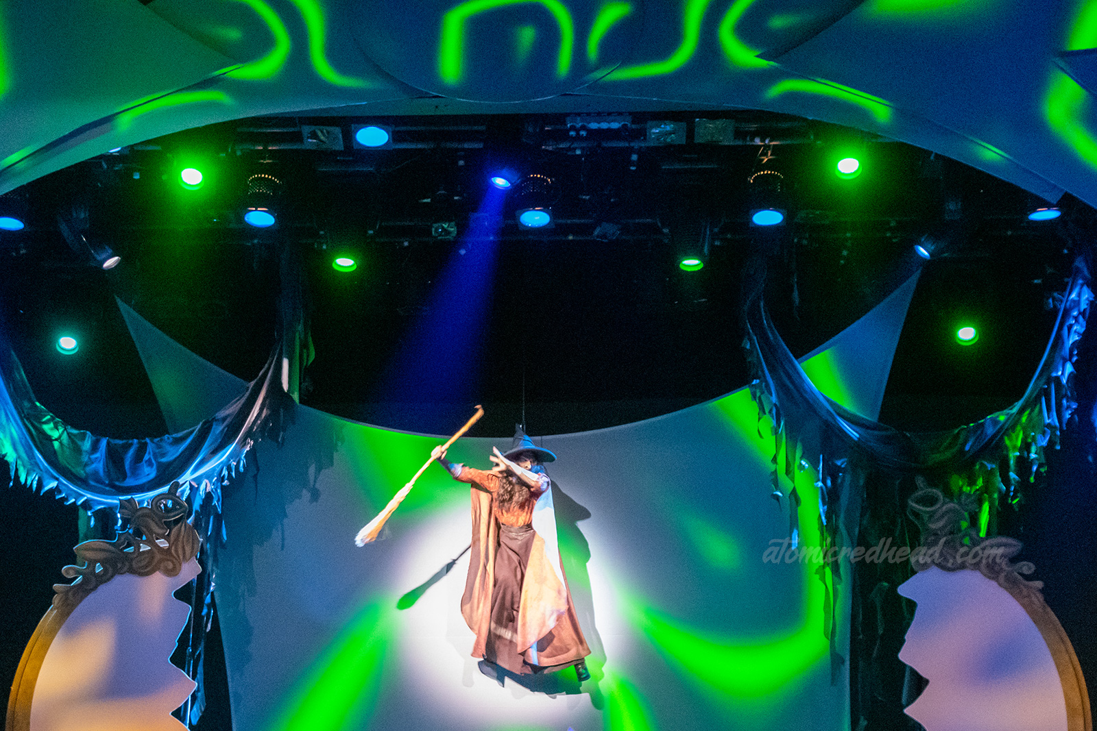 The Green Witch, also known as Sarah Marshall flies above the stage. She wears a long dress, with a billowing cape, a pointed witch hat and carries a broom.
