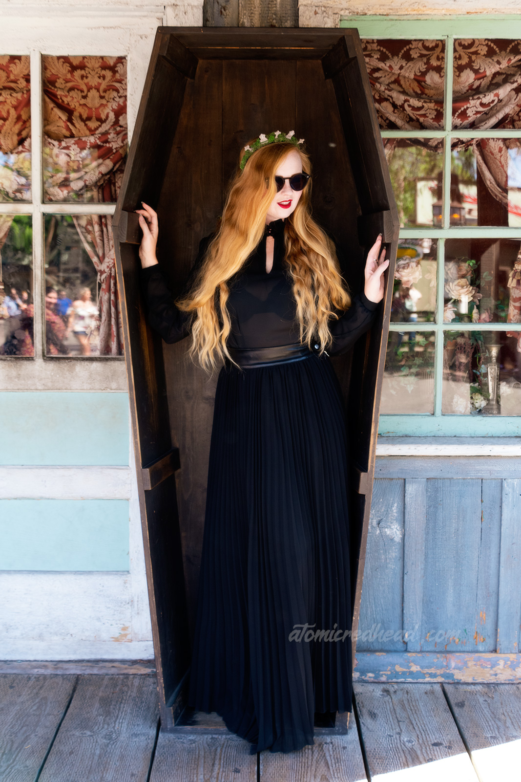 Myself, wearing a black long sleeve high collar blouse, and a long black skirt, and a tiara made of small tombstones, standing in the coffin sitting on the porch of the Undertaker.