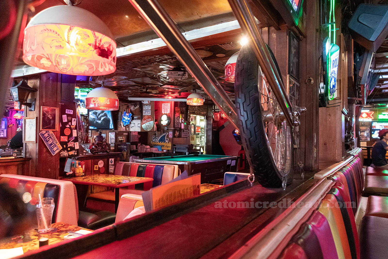 Interior. Various vintage lights advertising for beer hang from a newspaper covered ceiling. Wood paneled walls are covered in vintage signs, art, and license plates, the booths feature rainbow like upholstery.