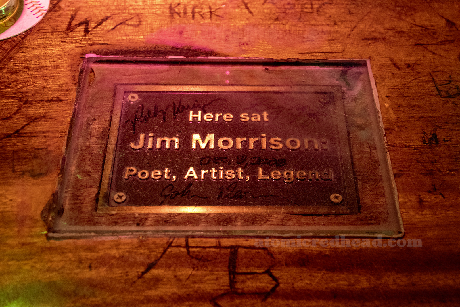 A bronze plaque is embedded in the bar and reads "Here sat Jim Morrison Poet, Artist, Legend"