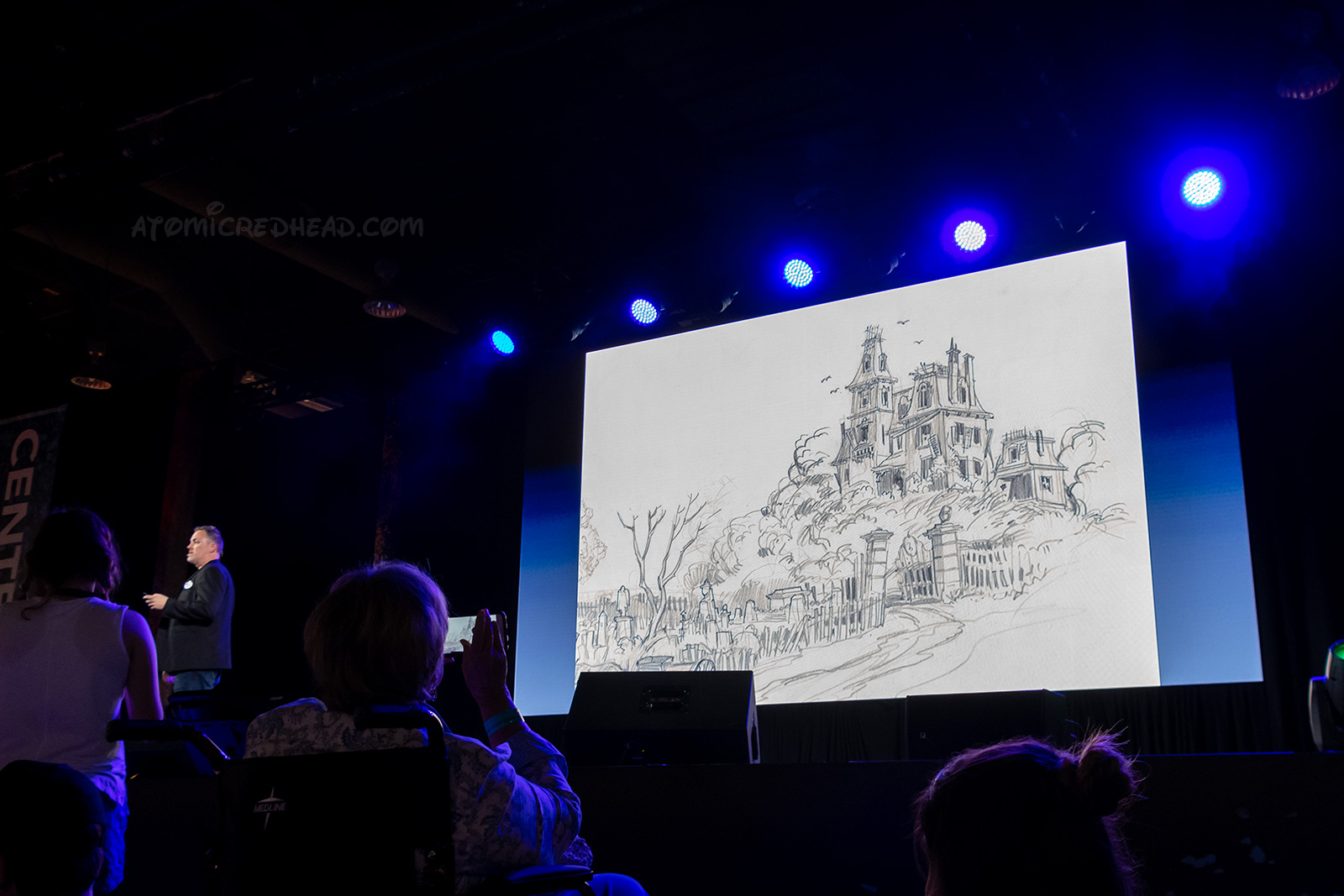 Christopher Merritt presents a panel on the Haunted Mansion and shows the very first concept art of the Haunted Mansion, which is a dilapidated Victorian. 