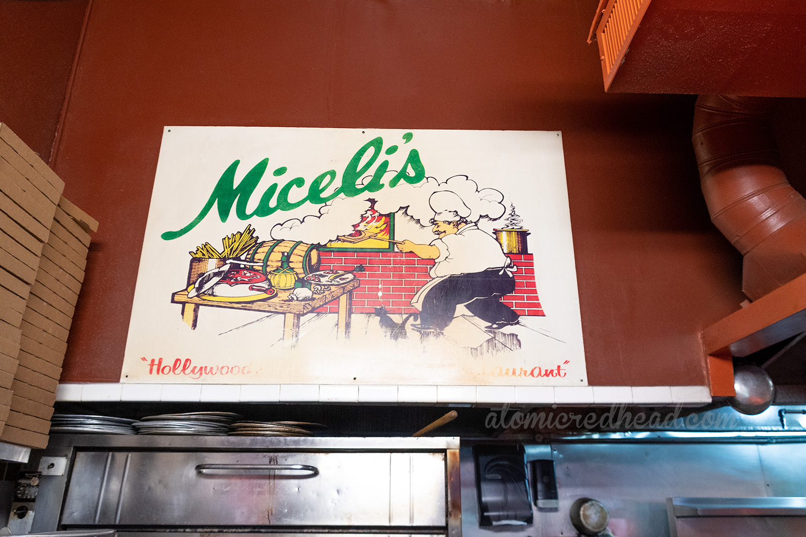 A large sign above the pizza ovens features a chef cooking, and "Miceli's" in green script.