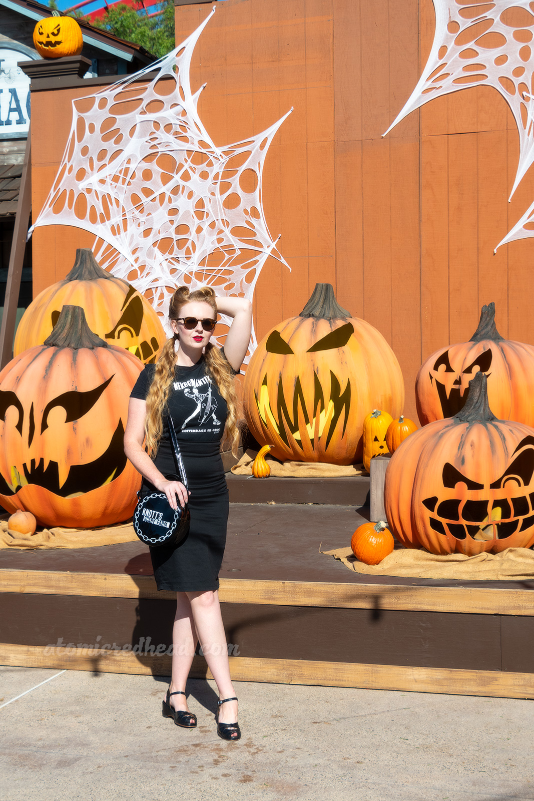 Myself, wearing a black t-shirt with a zombie playing an upright bass shaped like a coffin, and text reading "Nekromatix Coffinbass is Cool" and a black pencil skirt, standing in front of a stage with massive jack o'lanterns.