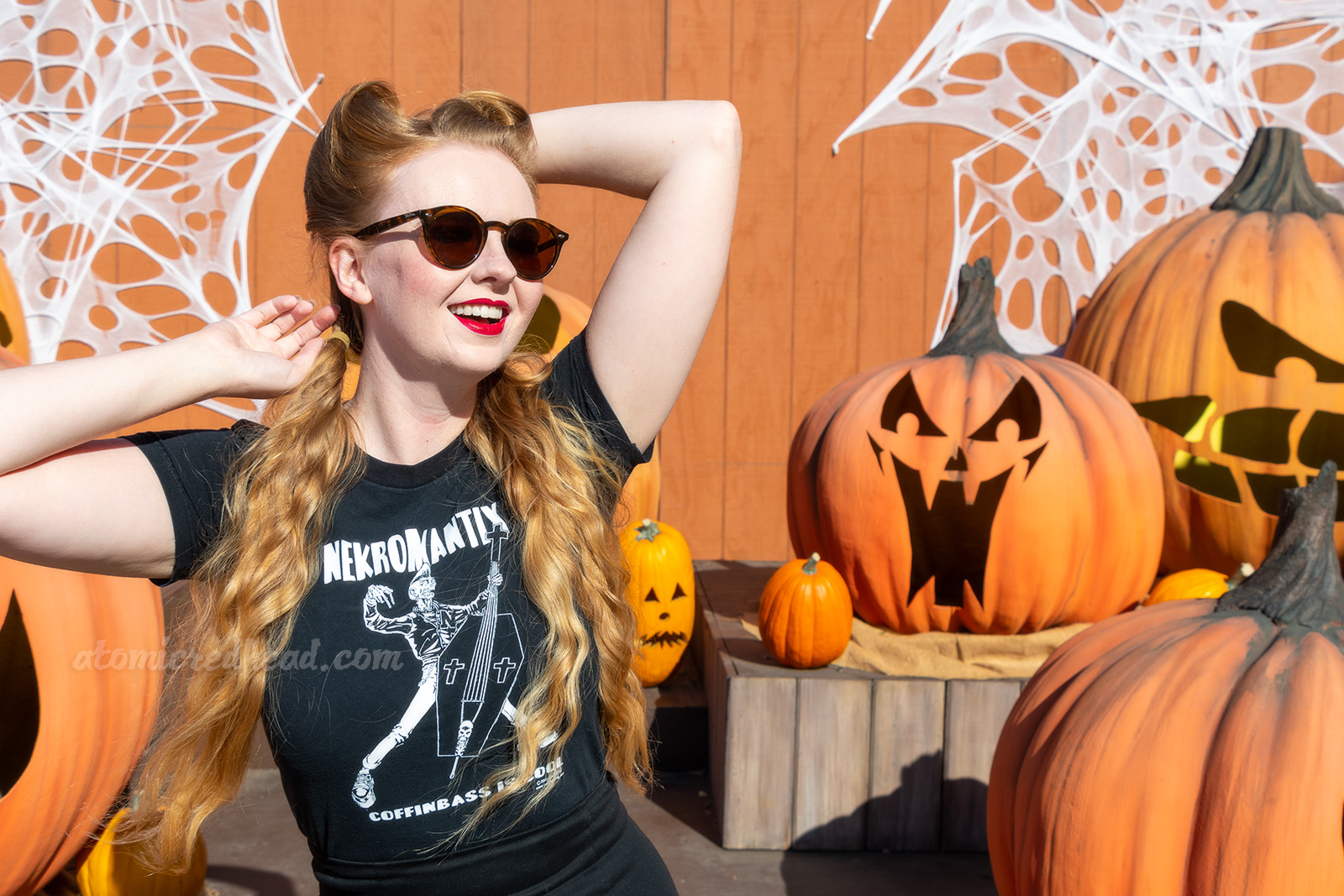 Myself, wearing a black t-shirt with a zombie playing an upright bass shaped like a coffin, and text reading "Nekromatix Coffinbass is Cool" and a black pencil skirt, standing in front of a stage with massive jack o'lanterns.