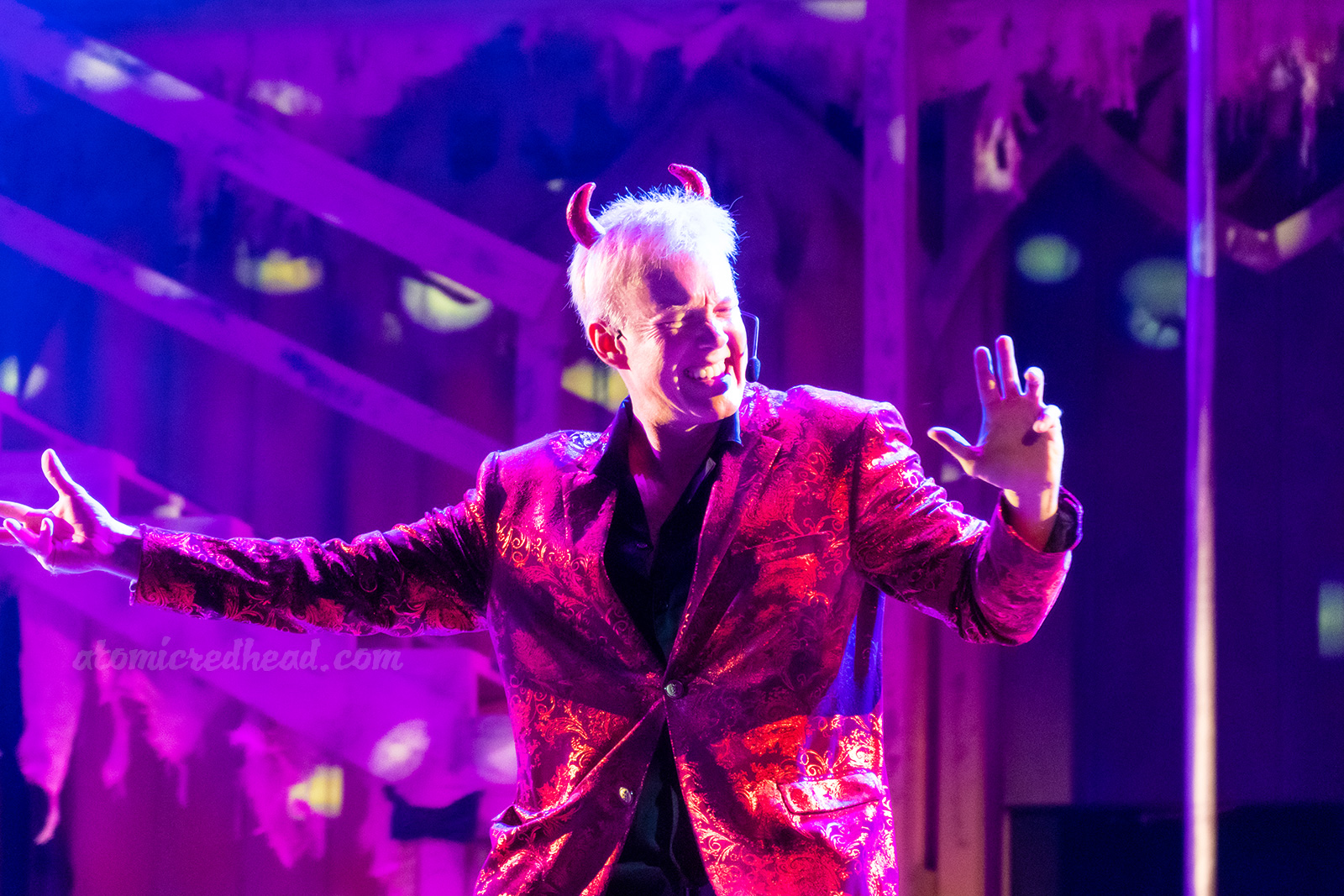 The devil, dressed in a red suit with small red horns, dances his way across the stage.