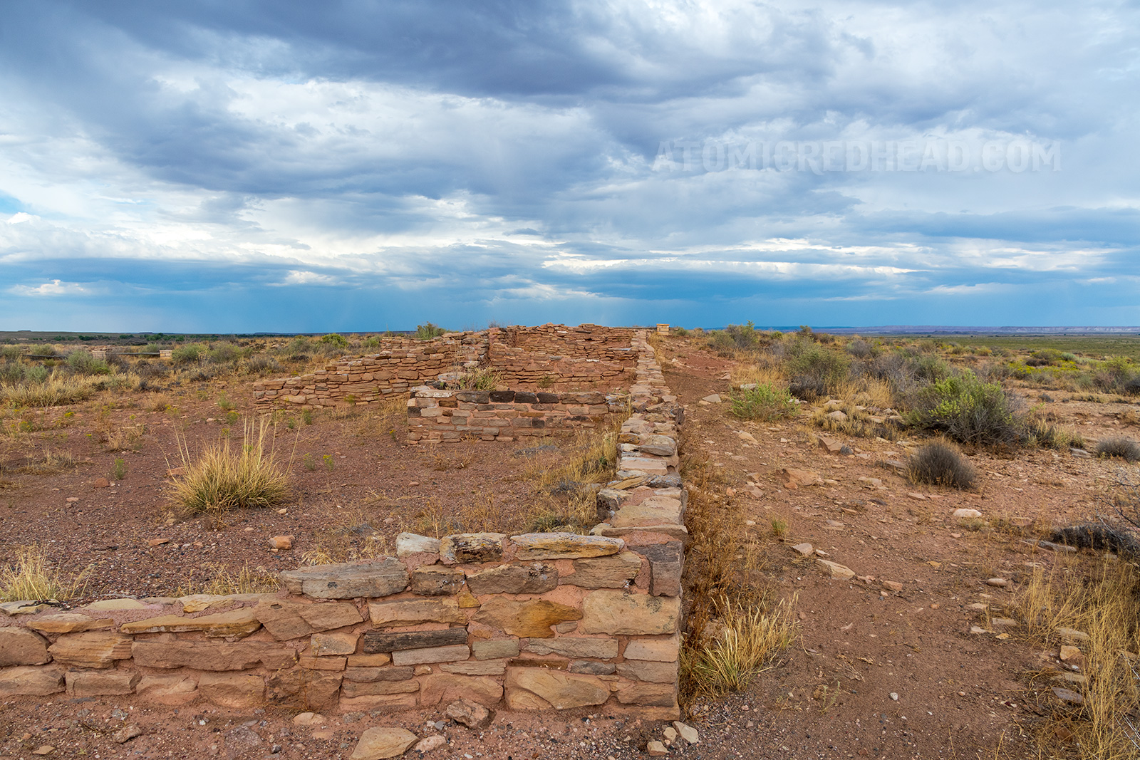 The ruin of an ancient dwelling. Several yellowish tan stones stacked on top of each other to form what is left of a wall. 