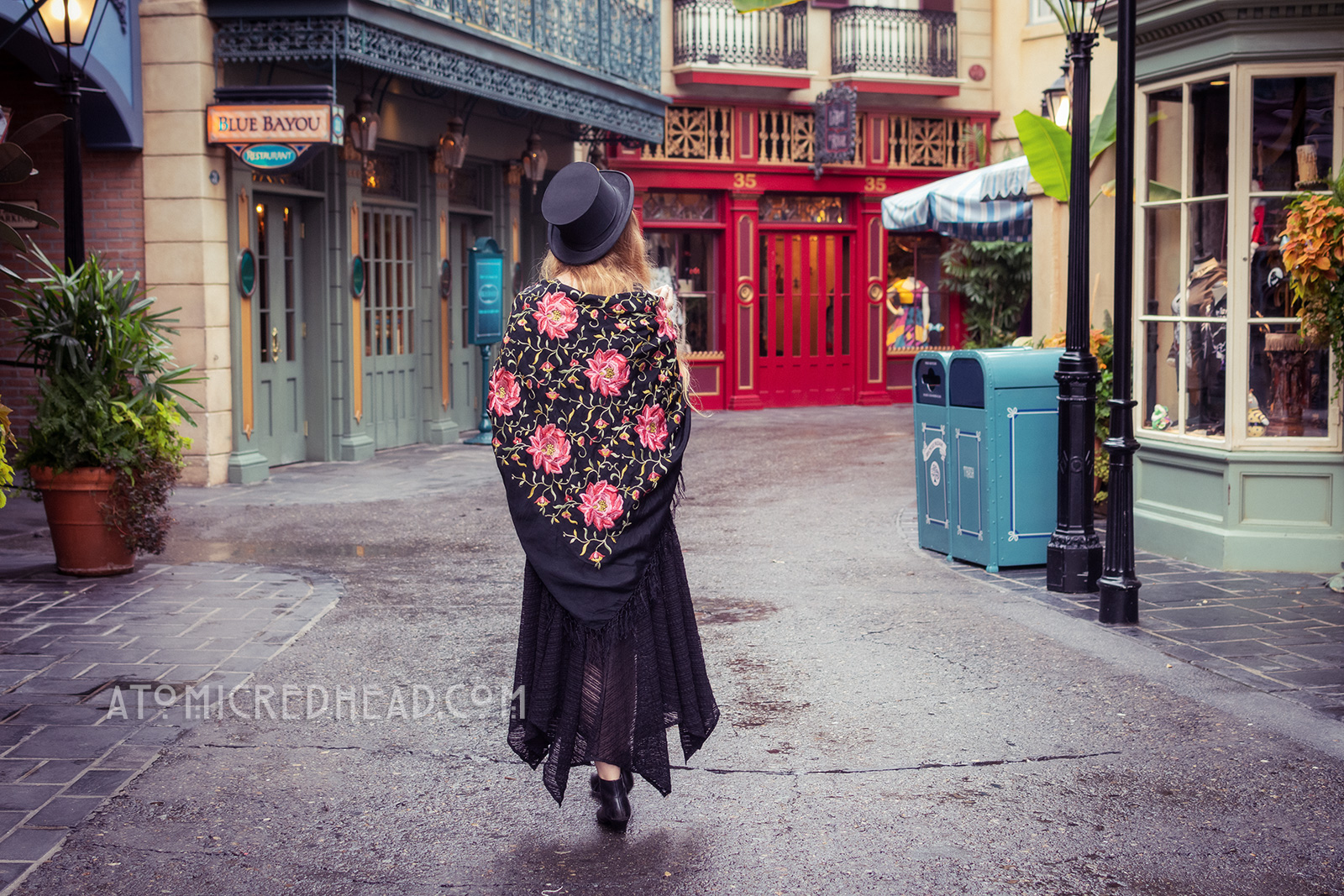 Myself, walking down one of the streets of New Orleans Square, a black top hat on my head, and a black shawl with pink embroidered flowers.