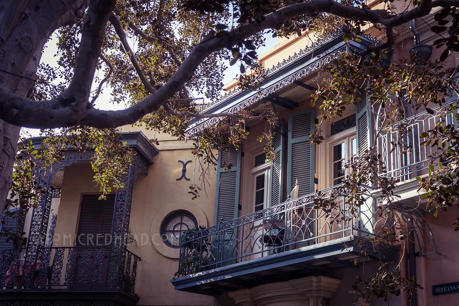 Teal shutters open out onto a small balcony where an easel and chair are set up. A portrait of a woman sits on the easel.