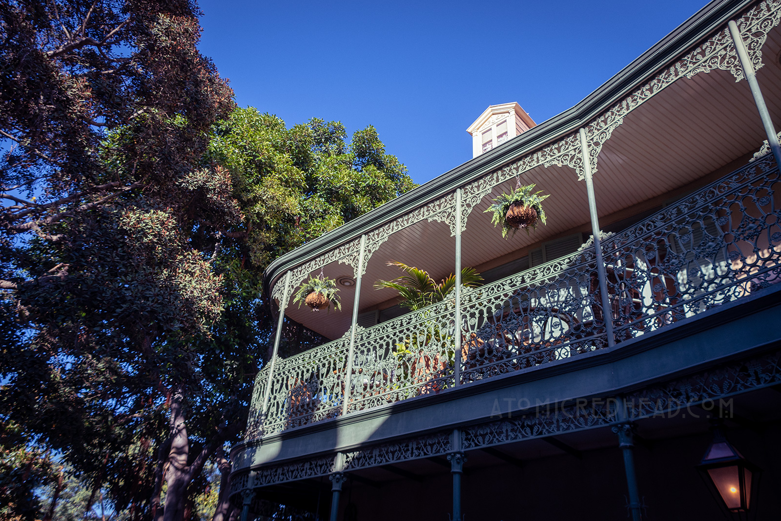 The sun lights up a pale green wrought iron balcony with wicker furniture sitting on it.