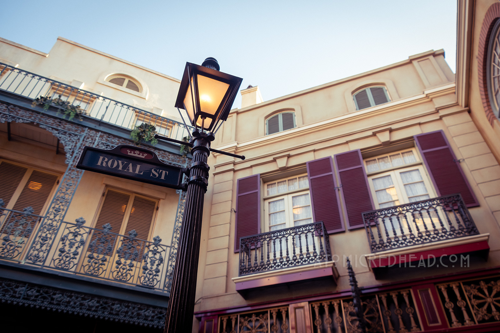 Maroon shutters on a butter colored two story building overlook Royal Street. A black metal lamppost features a street sign reading "Royal Street."