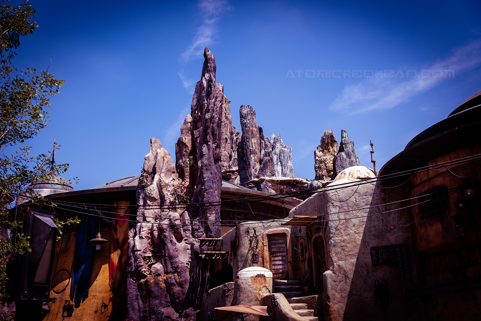 Rock spires stretch toward a blue sky. A small dwelling is nestled in the rocks.