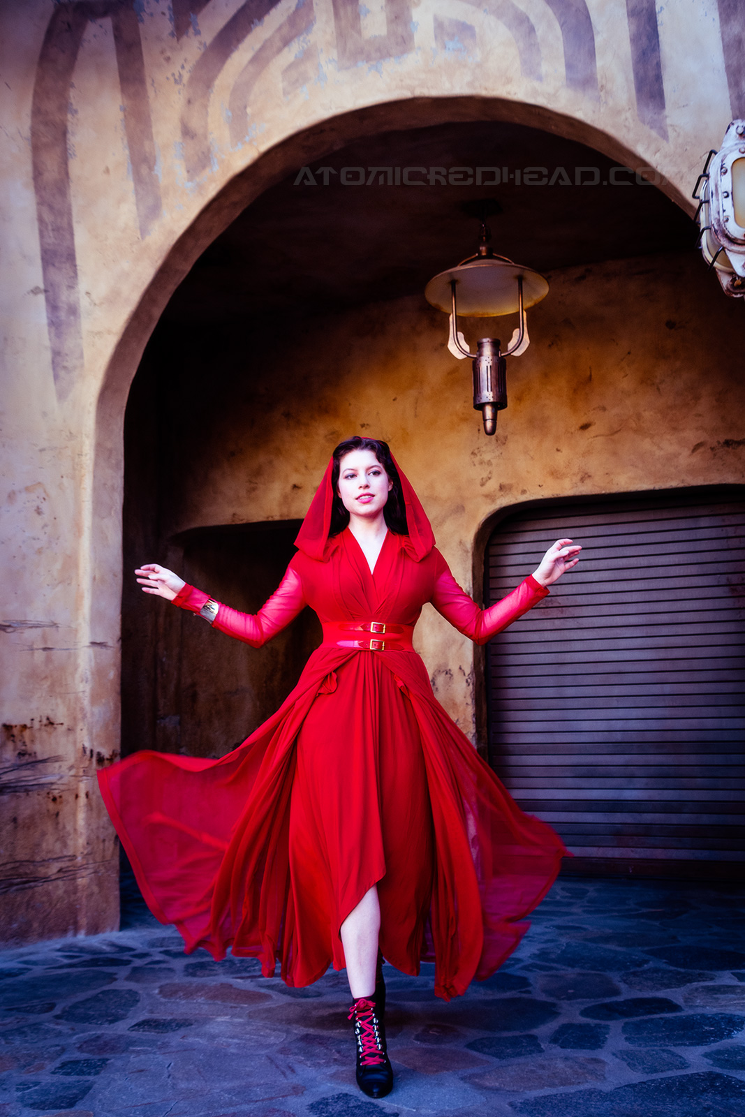 Solanah wears a crimson hooded robe with a double buckled belt. The robe flows behind her as she walks toward the camera.