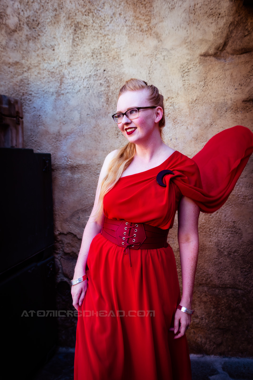 Myself wearing a full length red gown, it is asymmetrical with one shoulder ending in a short cape. A corset style belt at my waist, and a black crescent moon brooch at the shoulder.