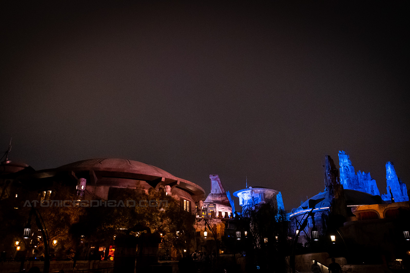 Star Wars: Galaxy's Edge features rounded buildings with dome roofs, lit up with blue and yellow lights at night.