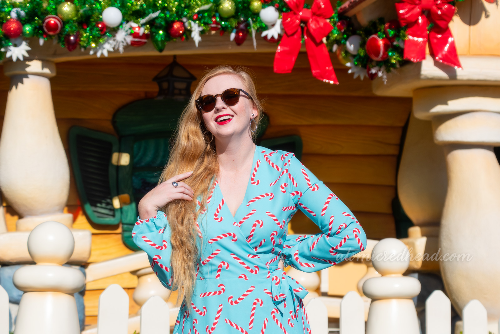 Myself standing in front of a brightly painted house, wearing a short, blue wrap dress with a red and white candy cane print on it.