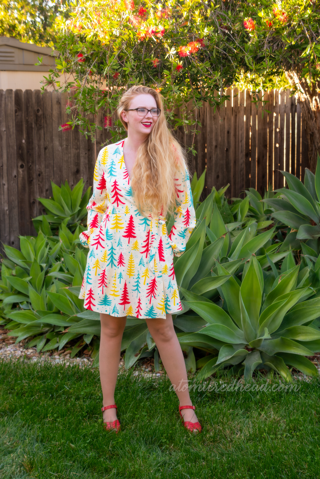 Myself, wearing an off-white short dress with yellow, red, and teal Christmas trees printed on it.