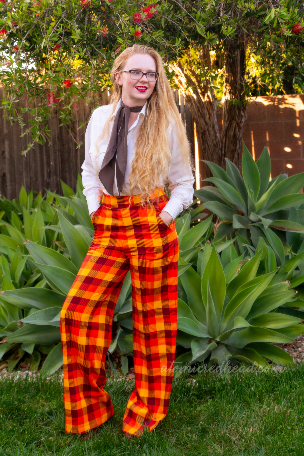 Myself, wearing a white western wear top, brown scarf, and yellow, orange, and brown plaid pants.