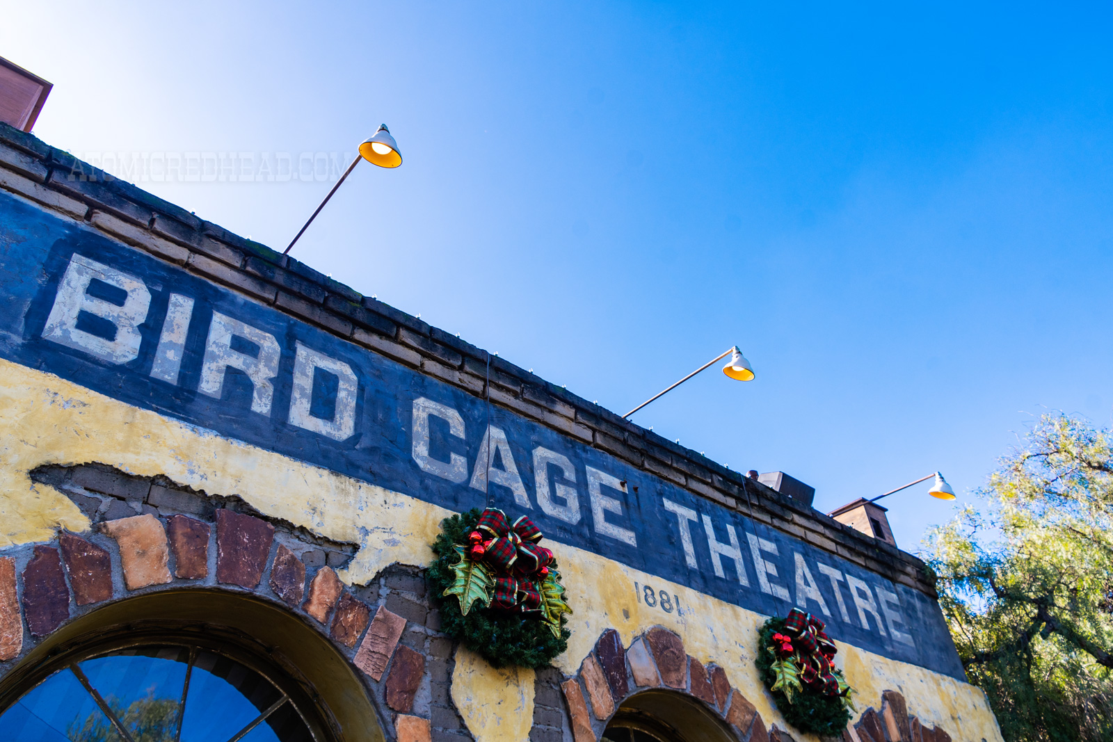 Exterior of the Bird Cage. A yellow adobe facade with arched doorways. The top is painted black with white letters reading "Bird Cage Theatre"
